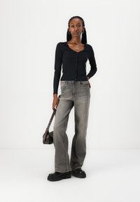Svart langermet knapp-up topp kombinert med grå flagrende jeans.antrekket er fullført med kraftige svarte støvler og en liten brun håndveske.