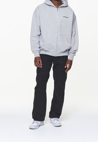 Grå zip-up hoodie med en framficka och logotyp. Svarta cargobyxor med flera fickor. Vita sportskor. Enkel, avslappnad outfit.