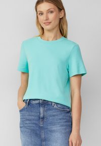 T-shirt en coton turquoise à manches courtes et col rond, associé à une jupe en denim bleu. Texture lisse, coupe décontractée.