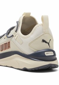 Zapatilla crema y marino que presenta material textil, cordones elásticos y una lengüeta trasera, con el logo de Puma y el acento "SOFTRIDE" en el talón.