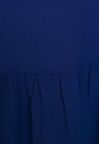 Tessuto blu con una superficie testurizzata, caratterizzato da una cucitura arricciata nella parte inferiore. Il tessuto appare leggero e ha una finitura stropicciata.