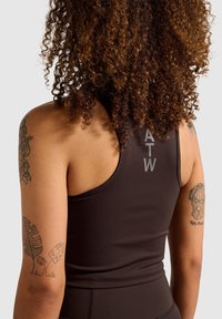 Brun athletisk tanktop med racerback-design. Har "ATW" logo i lys grå på ryggen. Glat tekstur og tætsiddende form.