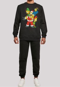 Persona vestida con sudadera negra y pantalones, la sudadera presenta a los personajes de Los Simpson vestidos con disfraces navideños.