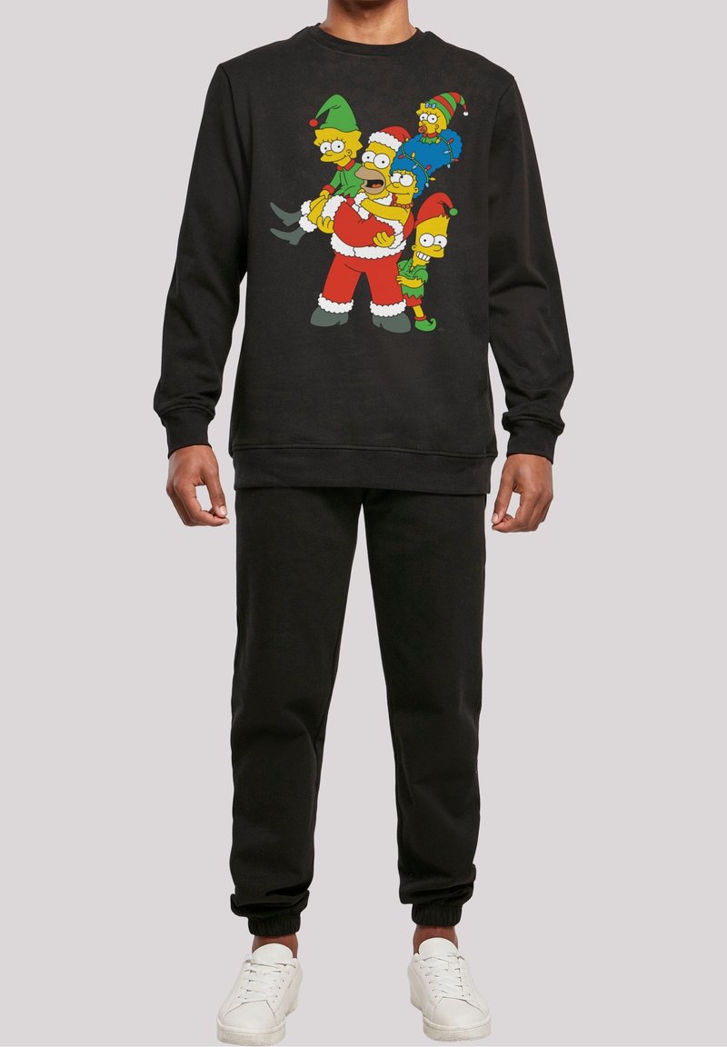 Persona vestida con sudadera negra y pantalones, la sudadera presenta a los personajes de Los Simpson vestidos con disfraces navideños.
