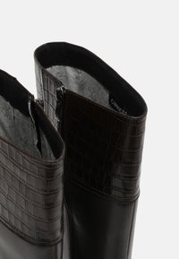 Botas de cuero marrón oscuro con un diseño texturizado de cocodrilo en la parte superior, que presentan un zipper lateral y un forro interior suave.