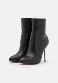 Bottines en cuir noir avec bout effilé, talon stiletto élevé et partie supérieure élastiquée. Texture lisse et design minimaliste.