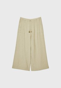 Pantalon beige à jambes larges avec ceinture élastique et cordons à pampilles à l’avant, avec de grandes poches avant visibles.