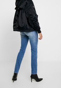 Giacca nera a maniche lunghe con cappuccio e dettagli elasticizzati, abbinata a jeans a sigaretta blu chiaro e stivaletti neri col tacco alto.
