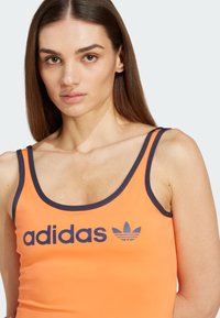 Oranje sporttanktop met marineblauwe accenten en logo. Heeft een ronde hals en een slim fit ontwerp. Gemaakt van een soepele, rekbare stof.