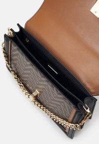 Borsa a mano nera e marrone con un motivo zebriato testurizzato, catena in oro e un interno liscio color tan. Presenta una chiusura magnetica.