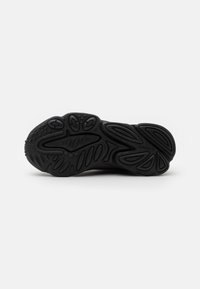 Black athletic shoe sole with textured rubber, featuring a wavy design and patterned traction elements for grip.