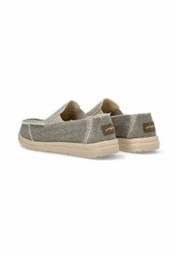 Zapatos slip-on fabricados en una tela gris texturizada con una suela de goma beige. El diseño presenta un perfil bajo y sin hardware visible.