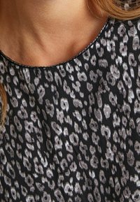 Top s leopardím potiskem v černé, šedé a bílé. Hladká látka s kulatým výstřihem a kontrastním lemováním. Disponuje volným střihem.