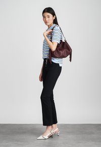 Blå og hvite stripete kortermet topp, svarte jeans, hvite slingback-heler og en liten burgunder håndveske med frynse detaljer.