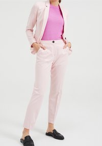 Ljusrosa kostym med en strukturerad kavaj och avsmalnande byxor, kombinerat med en texturerad magentafärgad topp och svarta slip-on skor.