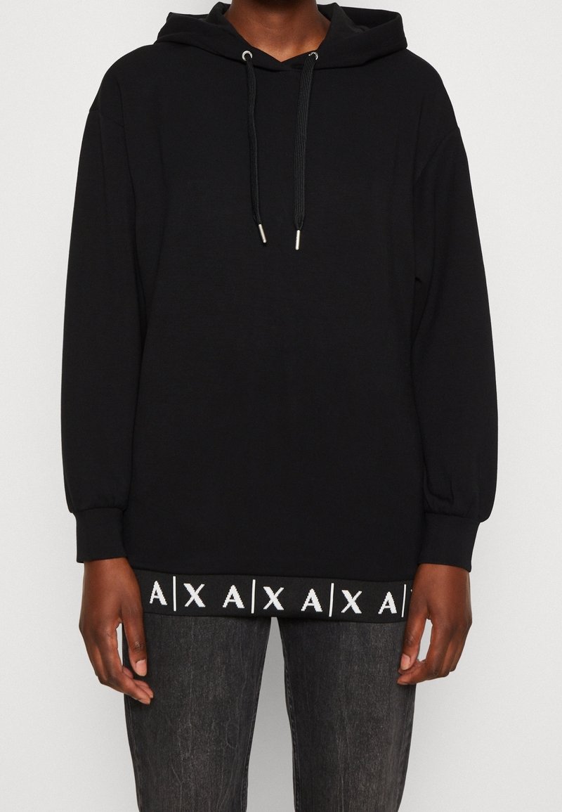 Černá mikina s kapucí, šňůrkami, dlouhými rukávy a žebrovaným lemem, na kterém je opakující se bílý vzor. Měkká tkanina, pohodlný střih.