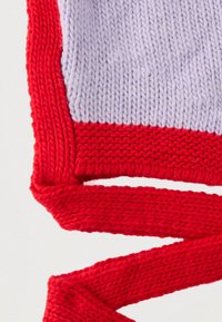 Accesoriu tricotat cu secțiuni mov și roșii; prezintă un design texturat, un fir gros și o margine și bretele contrastante roșii.