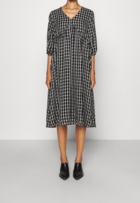 Abito midi a scacchi bianco e nero con scollatura a V e maniche a tre quarti, caratterizzato da una vestibilità ampia e dettagli arricciati. Indossato con scarpe nere a punta.