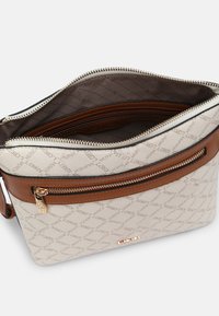 Borsa a tracolla rettangolare beige con accenti in pelle marrone, tasca anteriore con zip, tirazip dorato e scomparto principale aperto che mostra la fodera interna.