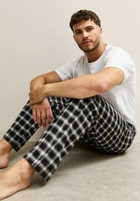 T-shirt blanc et pantalon de détente à carreaux noirs et blancs, coupe décontractée, posé sur une surface lisse et claire.