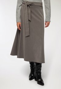 Szara spódnica o fasonie owijanym z wiązaniem w talii, wykonana z teksturowanej tkaniny, lekko rozszerza się u dołu, w połączeniu z czarnymi kozakiem na szpilce do kolan.