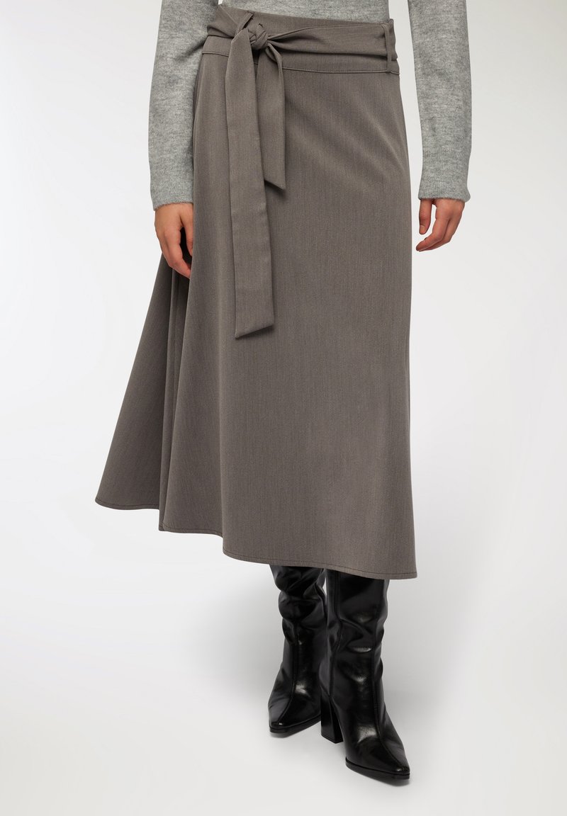 Szara spódnica o fasonie owijanym z wiązaniem w talii, wykonana z teksturowanej tkaniny, lekko rozszerza się u dołu, w połączeniu z czarnymi kozakiem na szpilce do kolan.