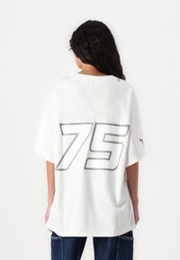 Hvit oversized jersey med korte ermer, har grå "75" på baksiden, mesh sideste paneler og logo aksenter nær skuldrene.