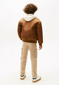 Brun polstret bomberjakke med et hvidt hættetrøje inderskjold, båret med beige cargo bukser med sidelommer og hvide sneakers.