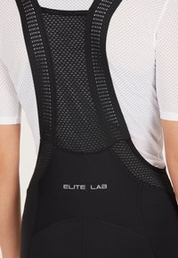 Mustat urheiluhousut, joissa on verkkoselkä, ruudukko-kuvio ja hopeinen "ELITE LAB" -logo, suunniteltu hengittävyyttä ja mukavuutta varten.