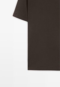 Rechterhelft van een donkerbruine T-shirt met korte mouwen op een witte achtergrond, met nette zoomsteken en een gladde stoftextuur.