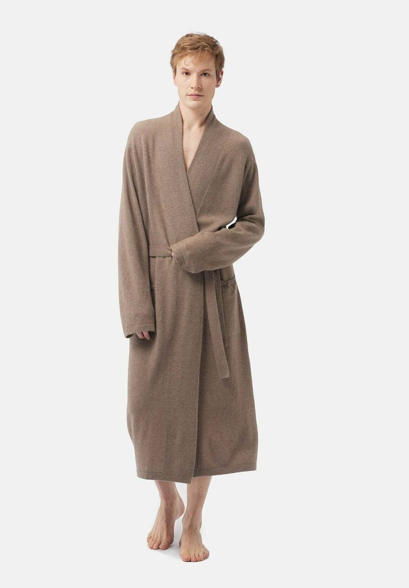 Brun, långärmad badrock gjord av mjukt tyg, med en omslagdesign, knytrem och två framfickor; modellen står barfota.