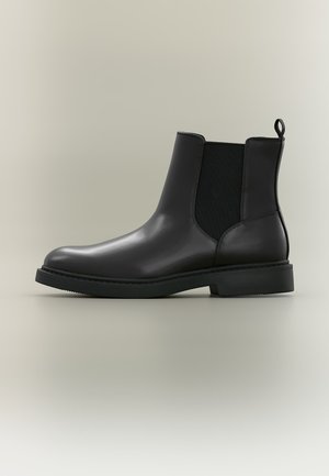 Schwarzer Leder-Chelsea-Stiefel mit elastischen Seitenteilen, Zuglasche hinten und einer niedrigen, langlebigen Gummisohle, vor neutralem Hintergrund dargestellt.