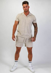 Beige kortärmad polo tröja med en ficka, matchad med shorts i samma färg. Vita hög-top sneakers med svarta och vita randiga strumpor.