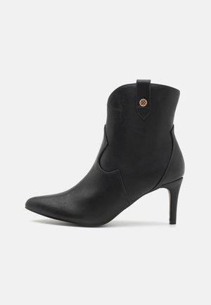 Black leather ankle boot with pointed toe, thin high heel, decorative top loop, and side stitching on a white background.