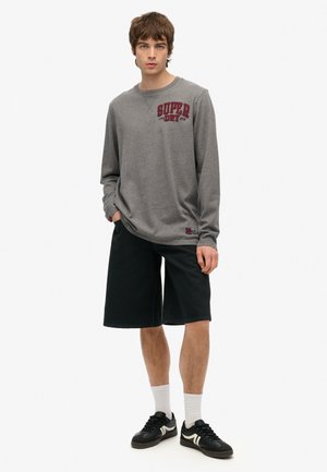 Grå langærmet skjorte med rød "SUPER DRY" tekst, parret med sorte shorts og sorte sneakers. Har en afslappet pasform og en uformel stil.