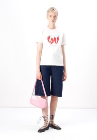 White t-shirt with red chili pepper graphic, paired with dark denim shorts and a pink croc-embossed handbag. Black lace-up flat shoes.