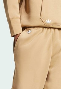 Beige hoodie and sweatpants set made of soft fabric with a smooth texture. Features white embroidered logo accents on both pieces.