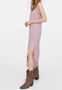 Helles Pink, ärmelloses Maxikleid mit seitlichen Schlitz und Spitzenbesatz; kombiniert mit braunen Cowboystiefeln, die einen Kontrast zum weichen Stoff bilden.