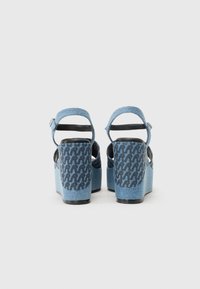 Denimplattformssandaler med en blå och svart mönstrad baksida, justerbart vristband och tjock, texturerad klack.