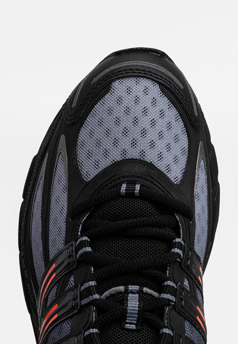 Scarpa sportiva nera e grigia con tomaia in rete, dettagli arancioni e motivo testurizzato. Presenta una suola imbottita e occhielli rinforzati.