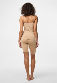 Bež majica brez rokavov in ujemajoče se kolesarske hlače iz gladkega, raztegljivega blaga. Dizajn ima tanke naramnice in oprijeto silhueto.