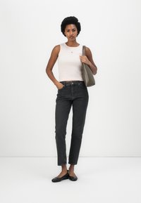 Top senza maniche rosa chiaro con un piccolo logo, jeans scuri a vita alta, scarpe nere basse e una borsa a tracolla grigia. Silhouette semplice e aderente.