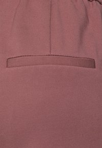 Tecido rosa com uma textura suave, apresentando um detalhe de bolso horizontal na cintura, cosido com uma linha da mesma cor.