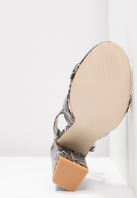 Sandale à talons hauts pour femmes avec des lanières en simili serpent et un talon bloc, présentée du côté de la semelle sur fond blanc.