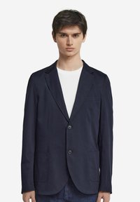 Mörkblå kavaj i lätt tyg, med två framfickor, en enda knappstängning och en kavaj med slag.