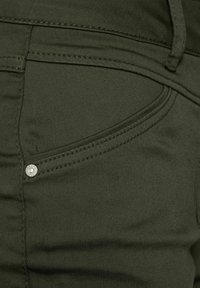 Tessuto in cotone verde oliva con una consistenza liscia, con tasche cucite e un accento in bottone metallico nella parte anteriore.