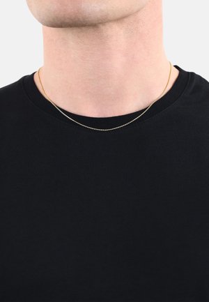 Collana a catena d'oro sovrapposta a una t-shirt nera a girocollo, con una texture liscia e una leggera lucentezza, che poggia appena sopra la clavicola.