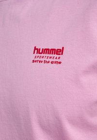 Rosa bomulds sportswear med "hummel" logo og "serve the game" tekst i rød broderi. Glat tekstur med et afslappet design.