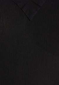 Tecido preto texturizado com uma aparência enrugada, apresentando um decote em forma de V e detalhes de costura subtis. Material suave e leve.