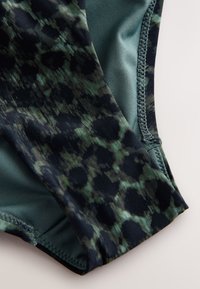 Close-up of dark green and black leopard print fabric with visible stitching on soft, smooth textile material.